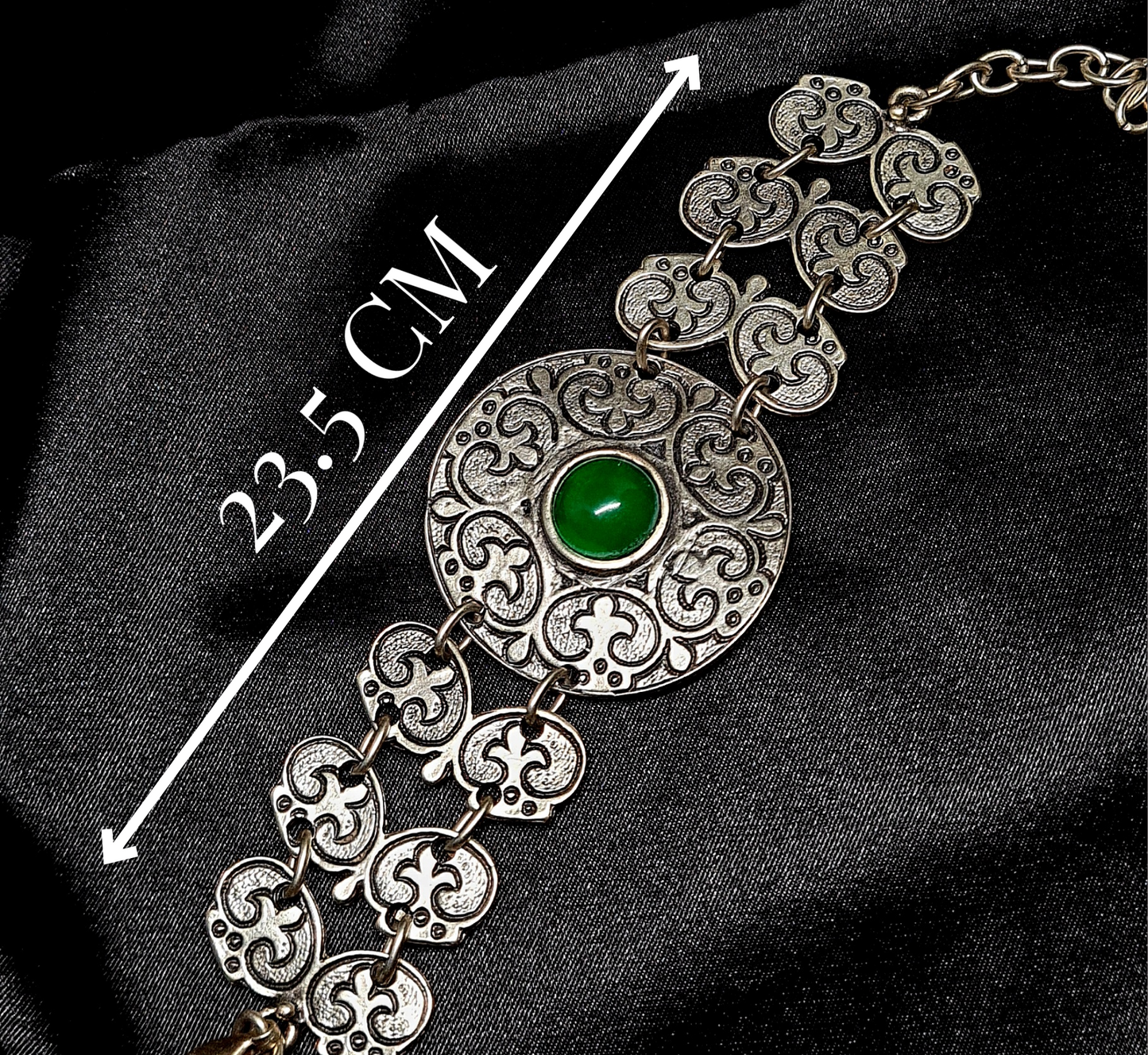 A silver bracelet with a green stone in the center. The bracelet is made of silver and has a delicate design. The green stone is oval-shaped and has a smooth finish with measurements 