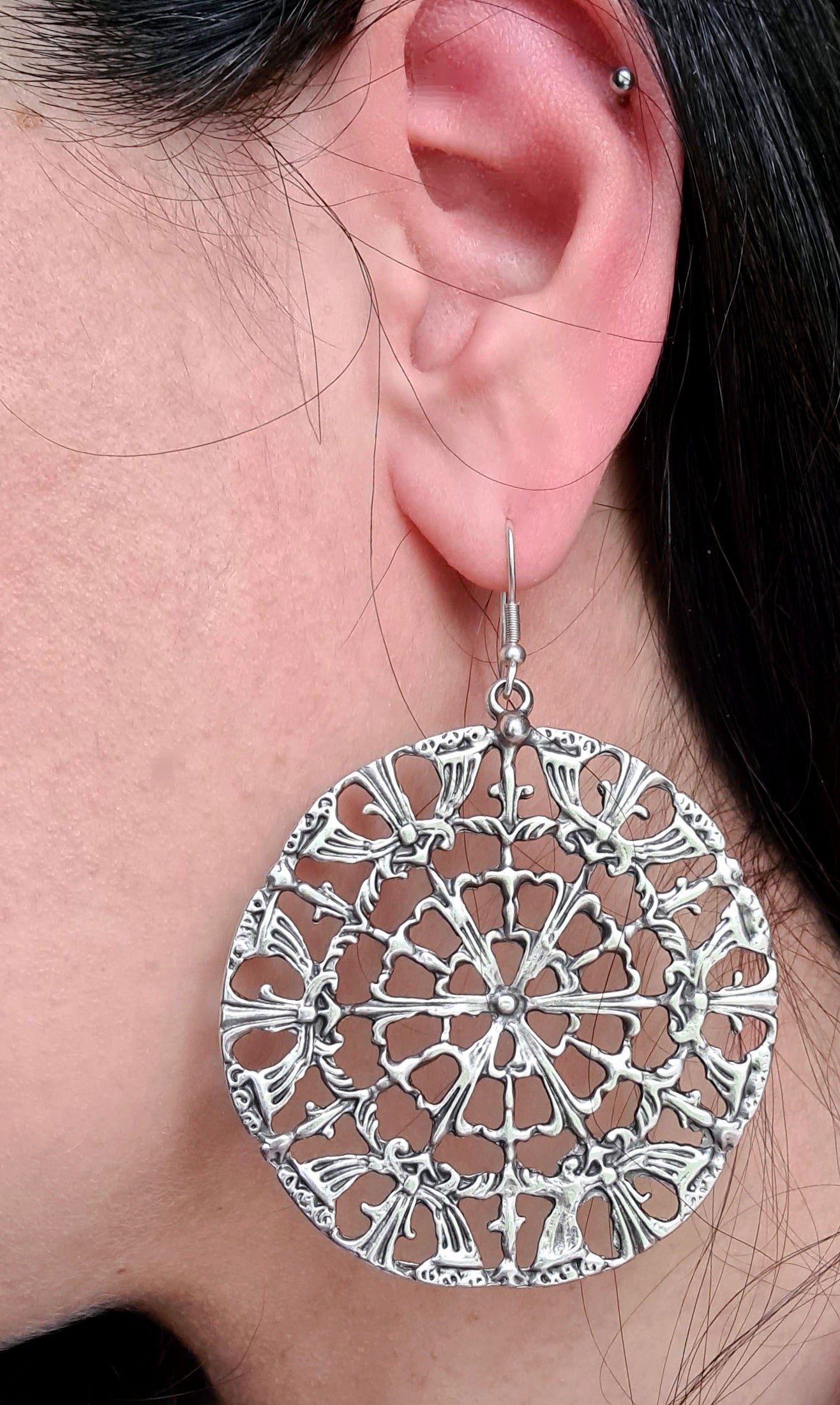 A woman wearing silver earrings. The earrings are small and delicate, and they have a circle design on them. The earrings are on the woman's ears, and they are reflecting the light.