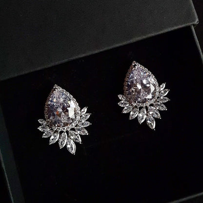 A pair of silver earrings with a large diamond in the center and a cluster of smaller diamonds around it. The earrings are sitting on a black table.