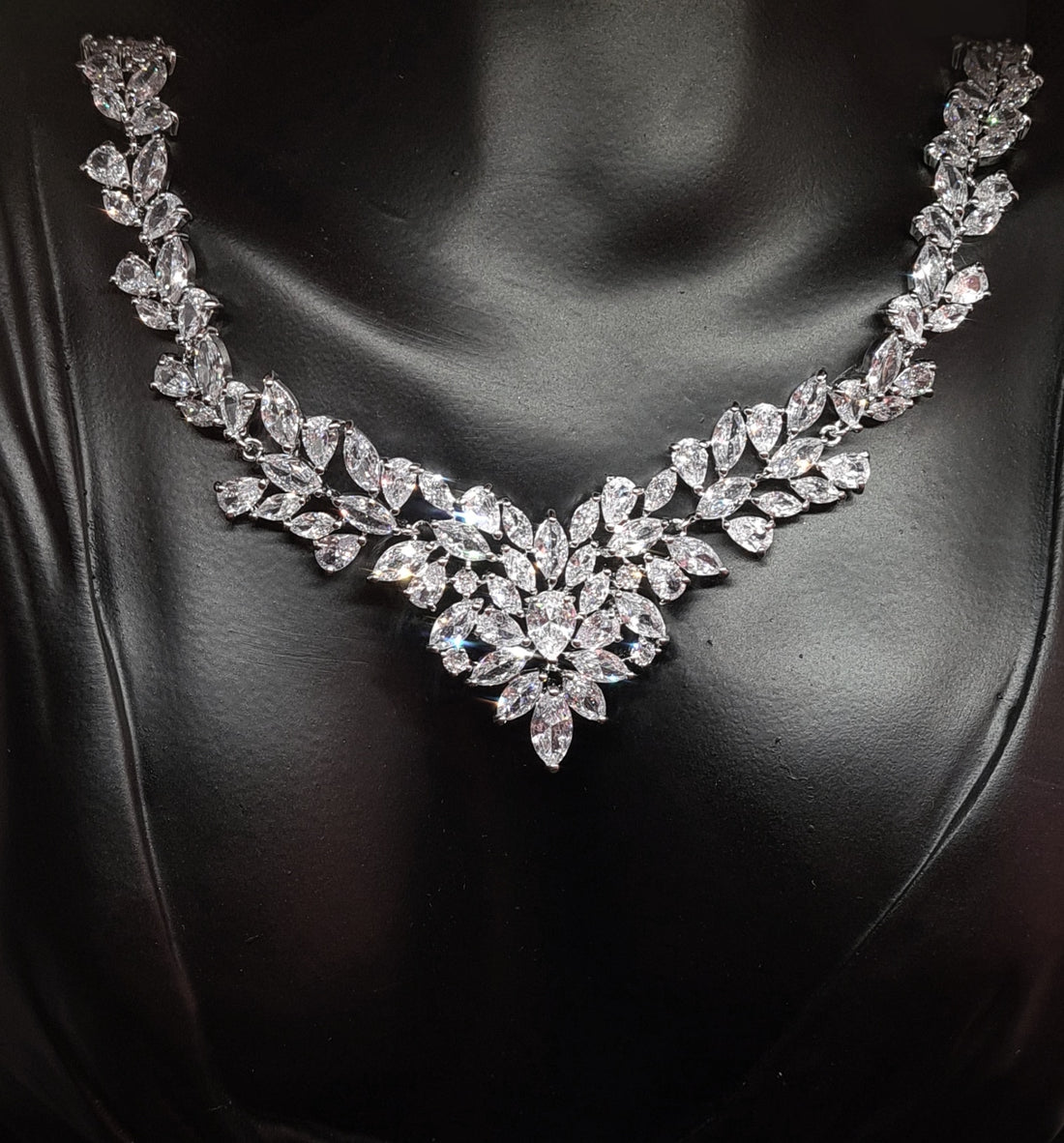 A close-up of a silver necklace with diamonds on it. The necklace is made of silver and has a delicate design. The diamonds are tear drop and sparkling. The necklace is sitting on a mannequin's neck.