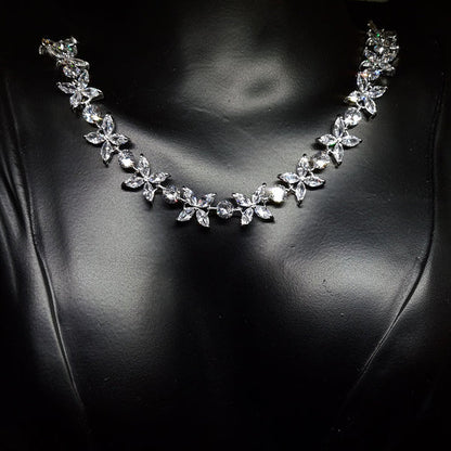Close-up of a necklace on a mannequin. The necklace is made up of multiple strands of cubic zirconia, with a large pendant in the center. The pendant is flower-shaped and has a sparkling cubic zirconia in the center. The necklace is resting on the mannequin's neck.