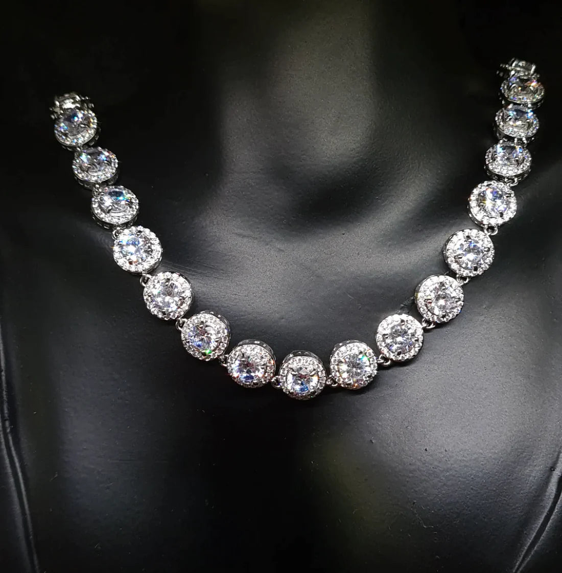 A mannequin wearing a necklace with diamonds. The necklace is made of silver and has diamonds in a round cut shapes and sizes. The cubic zirconia are the main focus of the image and they sparkle in the light.