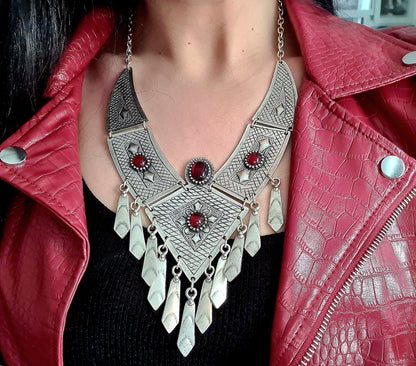a woman wearings A silver necklace with red stones on a black background. The necklace is made of silver and has a delicate design. The red stones are round and have a deep red color. The necklace is long and hangs down to the chest.