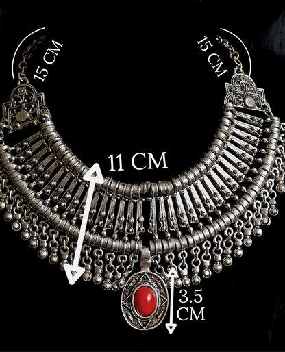 A silver and red necklace on a black background. The necklace is a long, filigree chain with a drop-shaped pendant. The pendant is made of silver and has a red stone in the center. The stone is a deep red color and has a polished finish. The background is a black velvet cloth. with measurements.