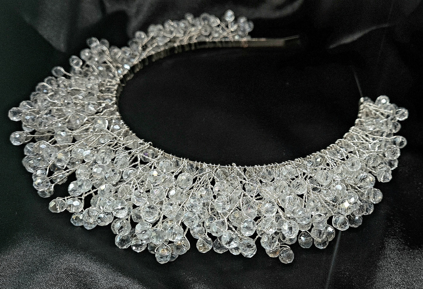 a bridal hair piece on a black background. The hair piece is made of pearls and crystals, and it has a delicate, feminine design. It is perfect for a bride who wants to add a touch of elegance to her wedding day look. The hair piece is shown on a black background, so the pearls and crystals stand out beautifully