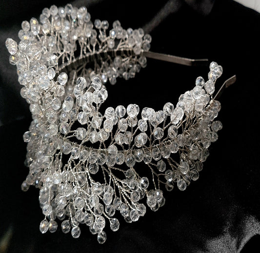 a bridal hair piece on a black background. The hair piece is made of pearls and crystals, and it has a delicate, feminine design. It is perfect for a bride who wants to add a touch of elegance to her wedding day look. The hair piece is shown on a black background, so the pearls and crystals stand out beautifully