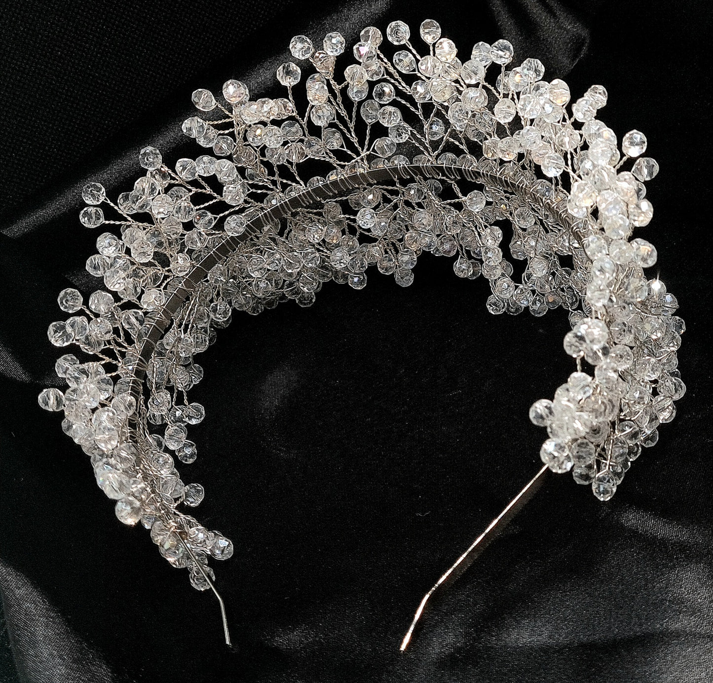 a bridal hair piece on a black background. The hair piece is made of pearls and crystals, and it has a delicate, feminine design. It is perfect for a bride who wants to add a touch of elegance to her wedding day look. The hair piece is shown on a black background, so the pearls and crystals stand out beautifully.