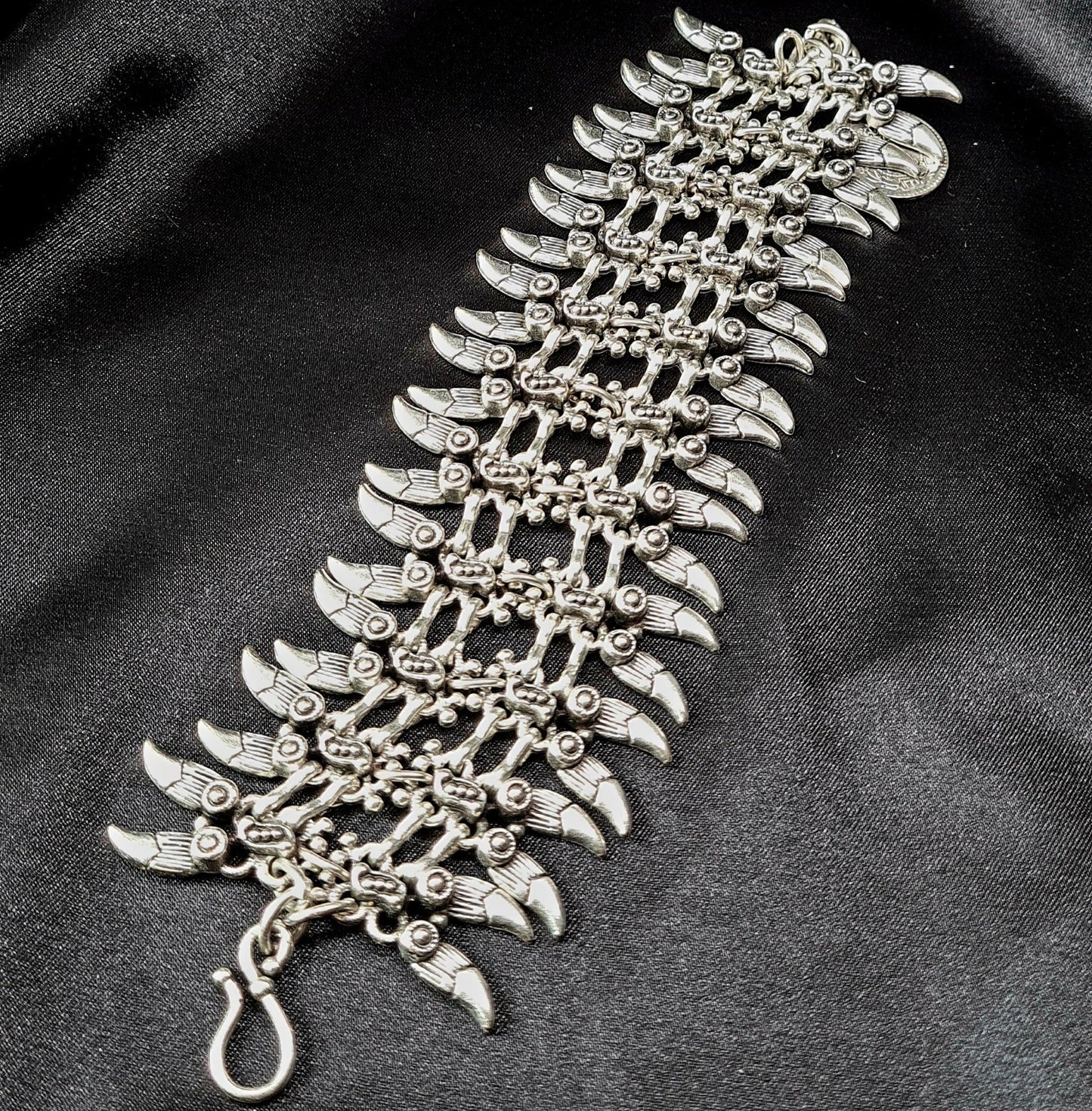 Professional studio shot of a wide artisan silver spike cuff bracelet with intricate bohemian engravings, displayed on a seamless matte black background for a luxury jewelry catalog.