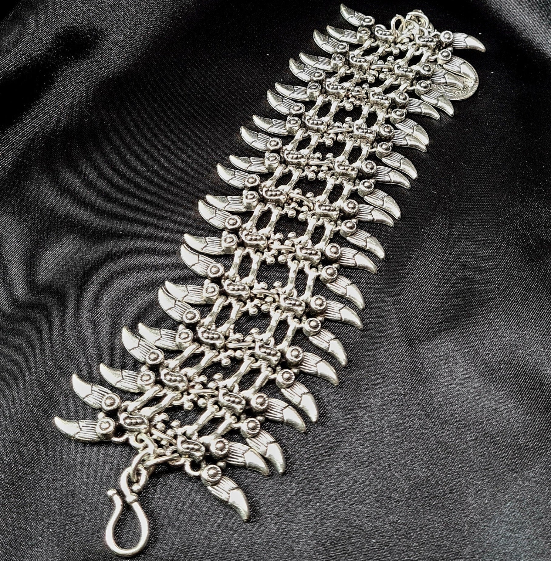 Professional studio shot of a wide artisan silver spike cuff bracelet with intricate bohemian engravings, displayed on a seamless matte black background for a luxury jewelry catalog.