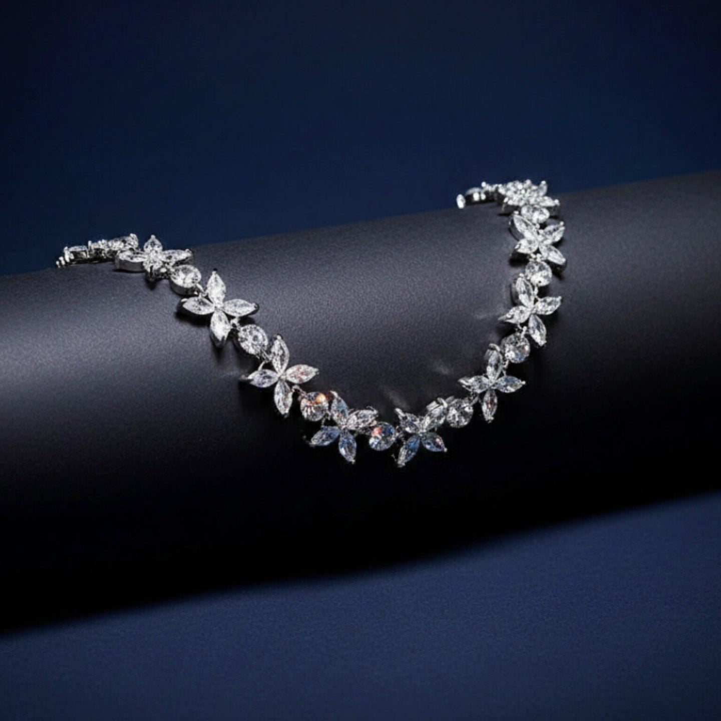 A brilliant diamond necklace featuring marquis-cut stones in a floral pattern, displayed elegantly draped over a matte black architectural cylinder against a deep blue background.