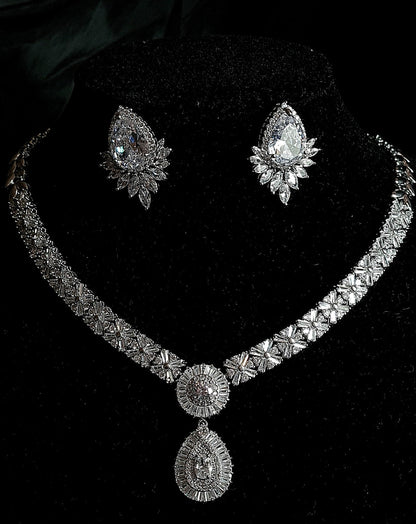 Sophisticated Black Mannequin Presenting a Cubic Zirconia Necklace and Earring Set with Intricate Design. The Necklace Features a Striking Central Teardrop CZ Stone, Surrounded by an Artful Arrangement of Smaller CZs. Complementing the Necklace, the Earrings Showcase Clustered CZs in a Dangle Drop Style. Against a Chic Black Background,
