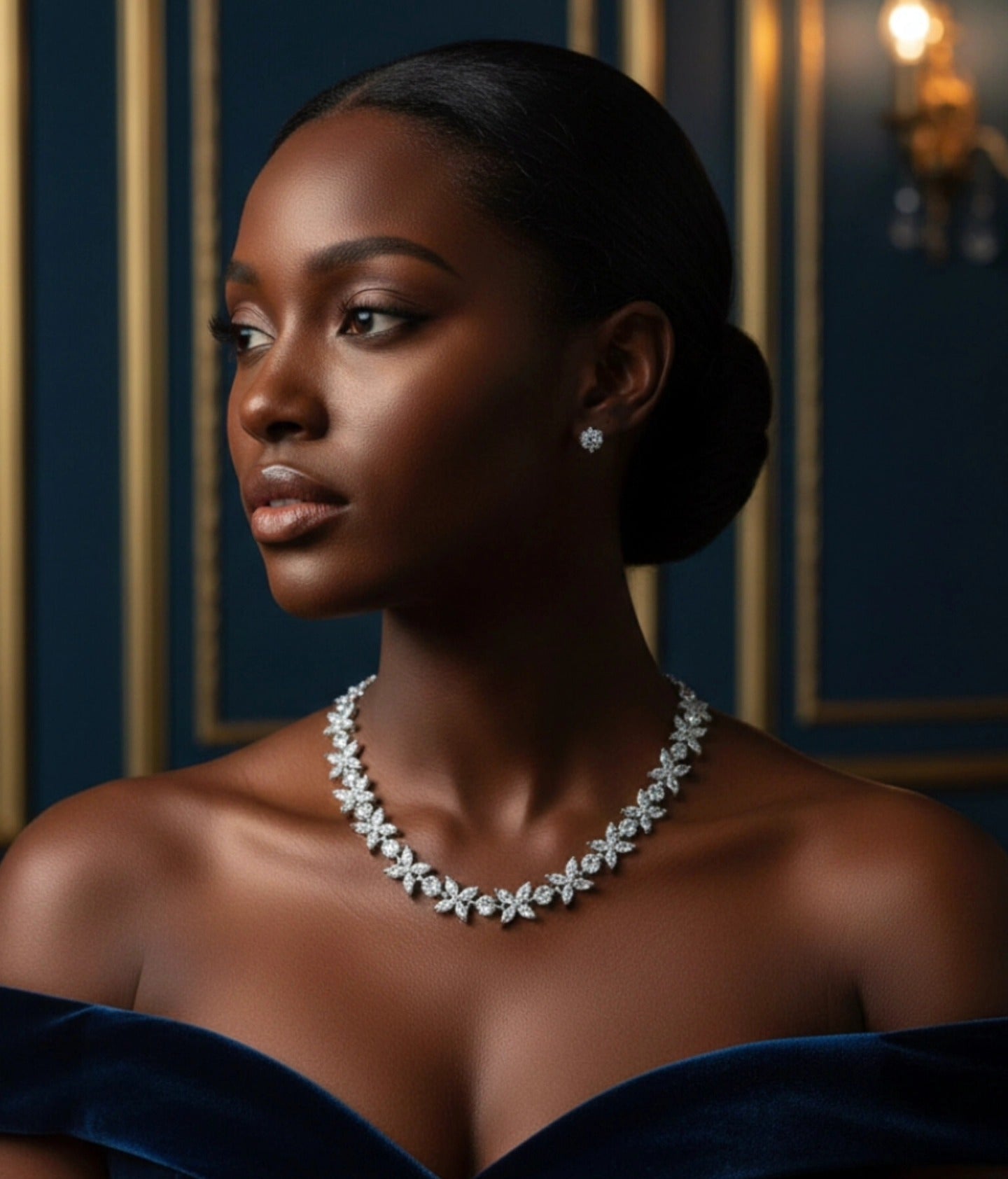 A high-fashion editorial portrait of a model with glowing skin wearing a diamond floral marquis necklace and matching stud earrings, styled in a navy velvet off-the-shoulder gown.