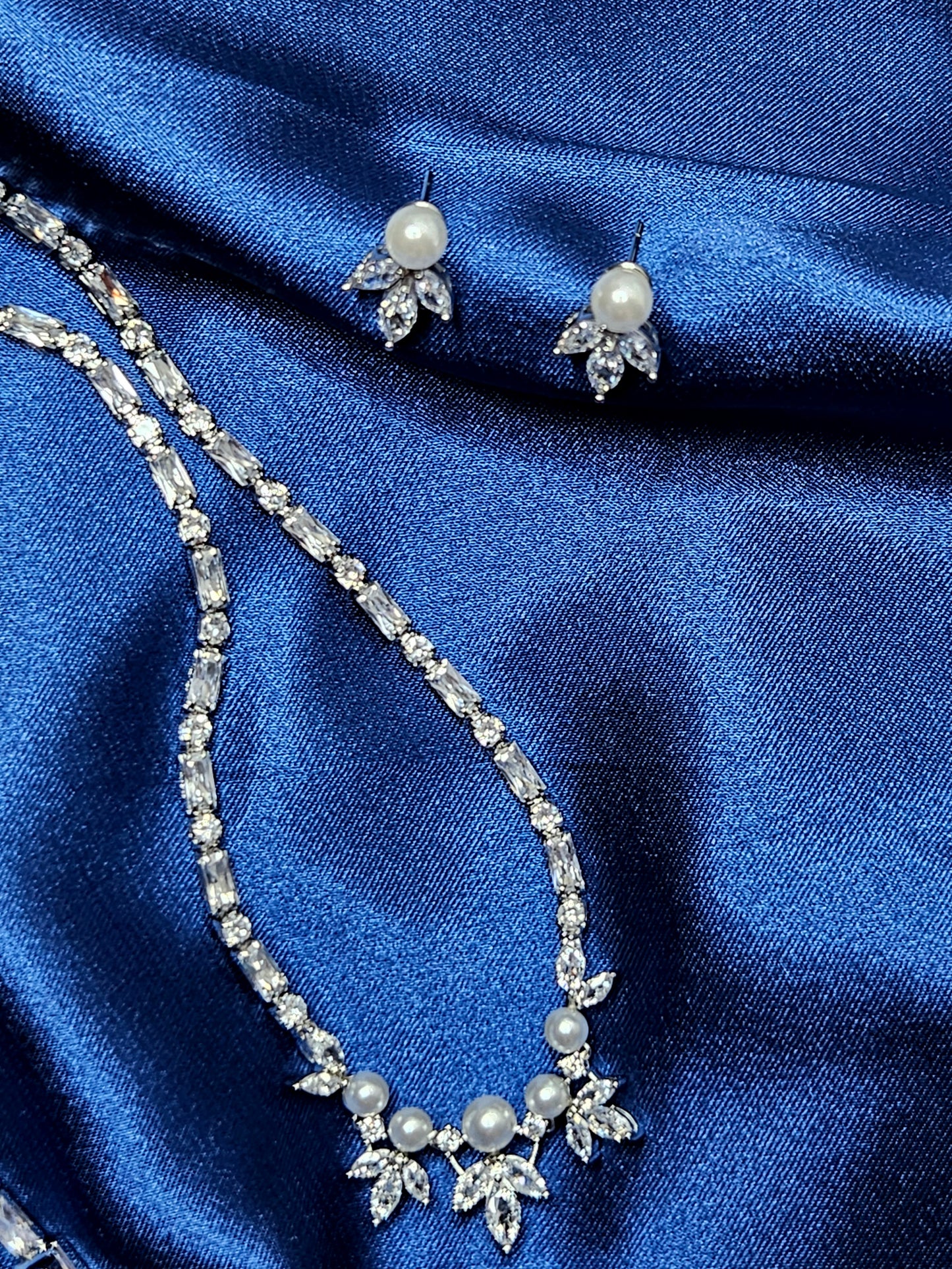 Detailed product shot of a high-end bridal jewelry collection featuring luminous pearls and brilliant-cut diamonds on draped royal blue silk.