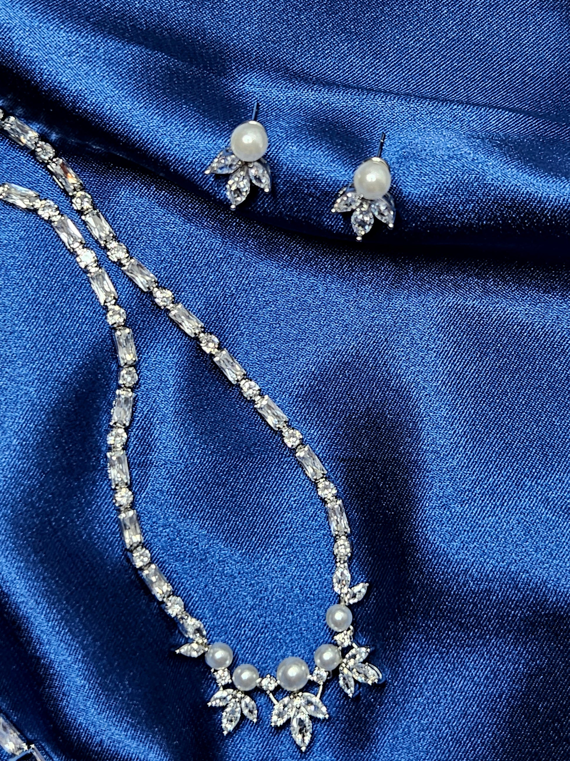 Detailed product shot of a high-end bridal jewelry collection featuring luminous pearls and brilliant-cut diamonds on draped royal blue silk.