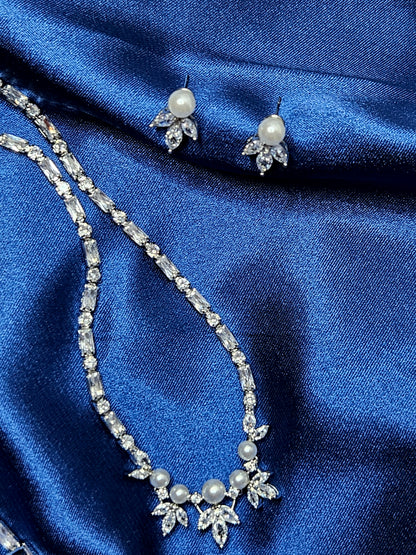 Detailed product shot of a high-end bridal jewelry collection featuring luminous pearls and brilliant-cut diamonds on draped royal blue silk.