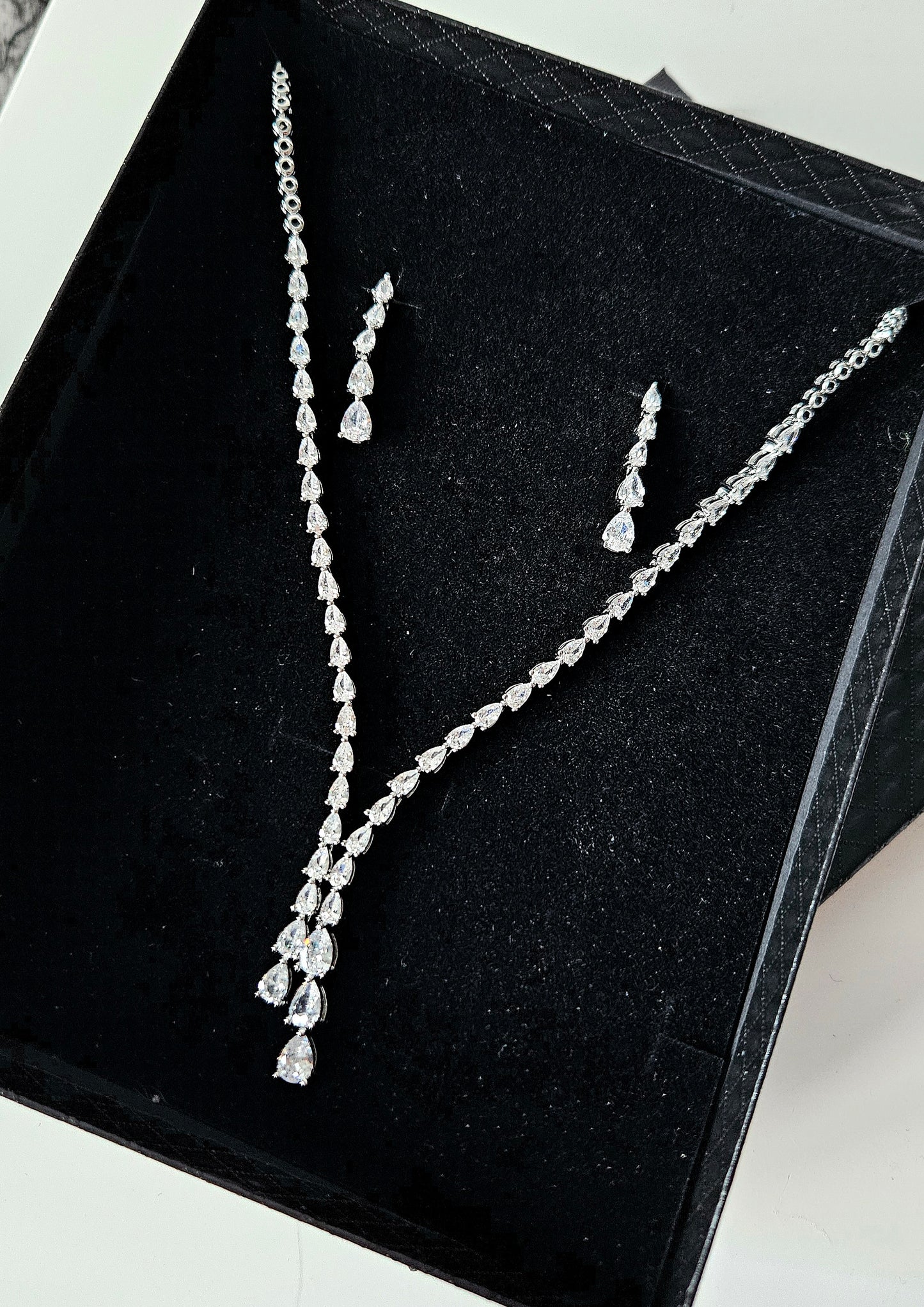 The Dilara Jewelry Set by La Pasión displayed on black box. This silver ensemble features a 44.45 cm botanical vine necklace with a 3.81 cm pear-cut drop and matching 3.18 cm x 0.64 cm marquise earrings, highlighting the brilliant craftsmanship and premium finish.