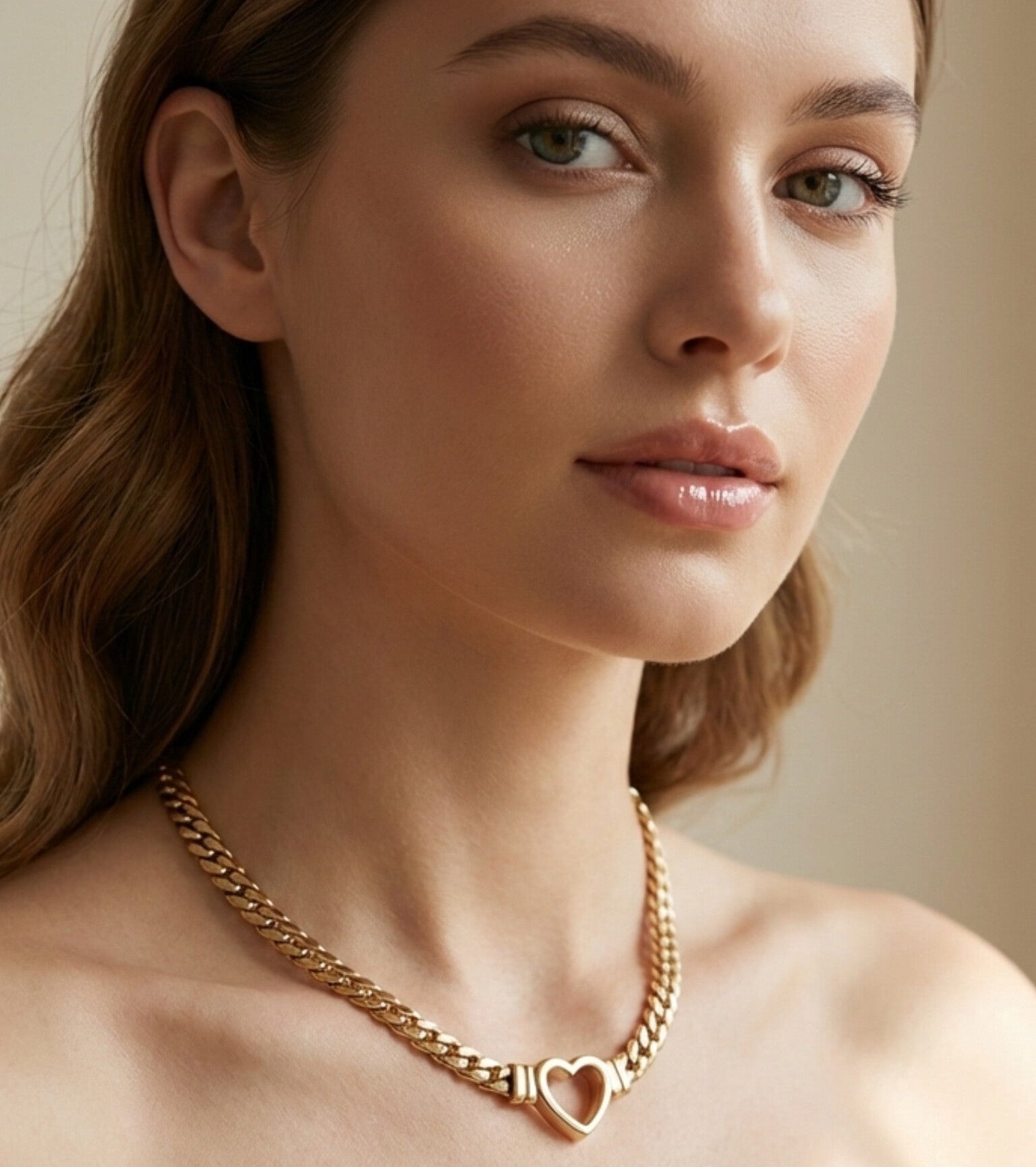 A high-fashion, editorial close-up of a model with soft wavy hair showcasing a premium gold curb chain necklace. The design features a central high-polish open-heart connector, radiating an elegant, sophisticated, and fashion-forward aesthetic for the La Pasión flagship brand.