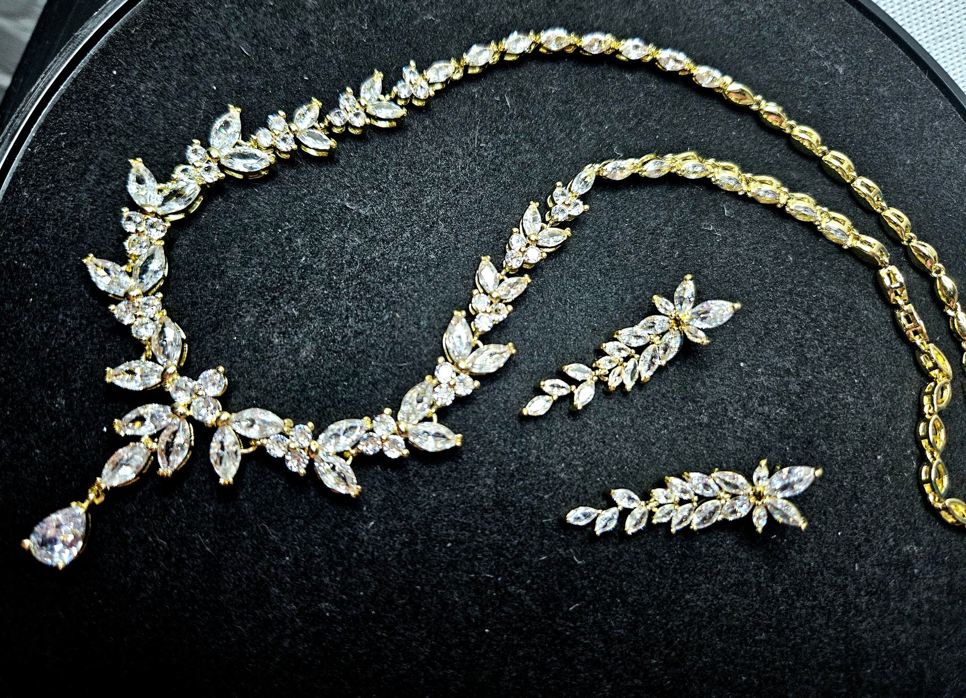 An editorial overhead shot of the La Pasión Regal Gold Jewelry Set, featuring a marquise-cut vine necklace and matching earrings on a dark, textured background. The gold-tone finish and brilliant stones evoke a sense of high-status luxury and craftsmanship.