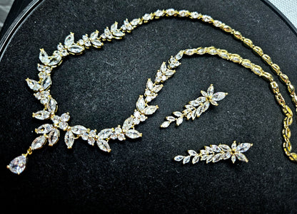 An editorial overhead shot of the La Pasión Regal Gold Jewelry Set, featuring a marquise-cut vine necklace and matching earrings on a dark, textured background. The gold-tone finish and brilliant stones evoke a sense of high-status luxury and craftsmanship.