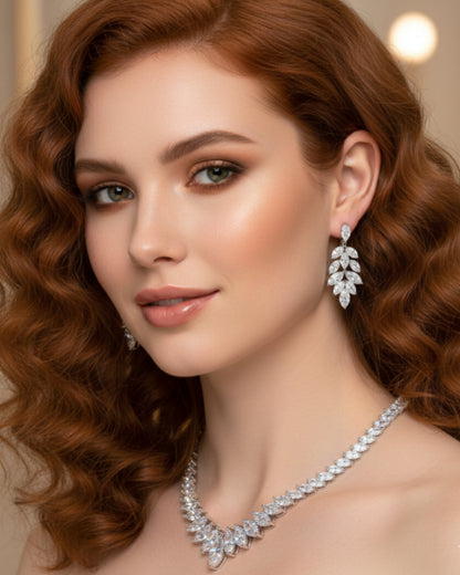 Close-up editorial portrait of a model with elegant wavy auburn hair wearing a high-end marquise-cut diamond necklace and matching leaf-style drop earrings against a warm, blurred luxury backdrop.