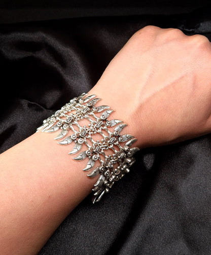 Extreme macro photography of the artisan silver spike cuff bracelet on a model's wrist, focusing on the fine engraved details, the metallic spikes, and the high-contrast play of light and shadow.