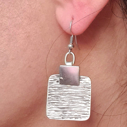 Extreme close-up macro shot of a textured square silver earring on a model's ear, showcasing the intricate craftsmanship and elegant metallic finish