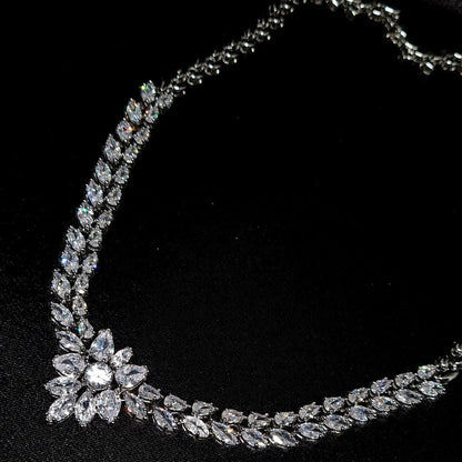 A high-detail shot of a silver-toned necklace featuring a double row of marquise-cut diamonds leading to a central floral cluster, set against a black silk background.