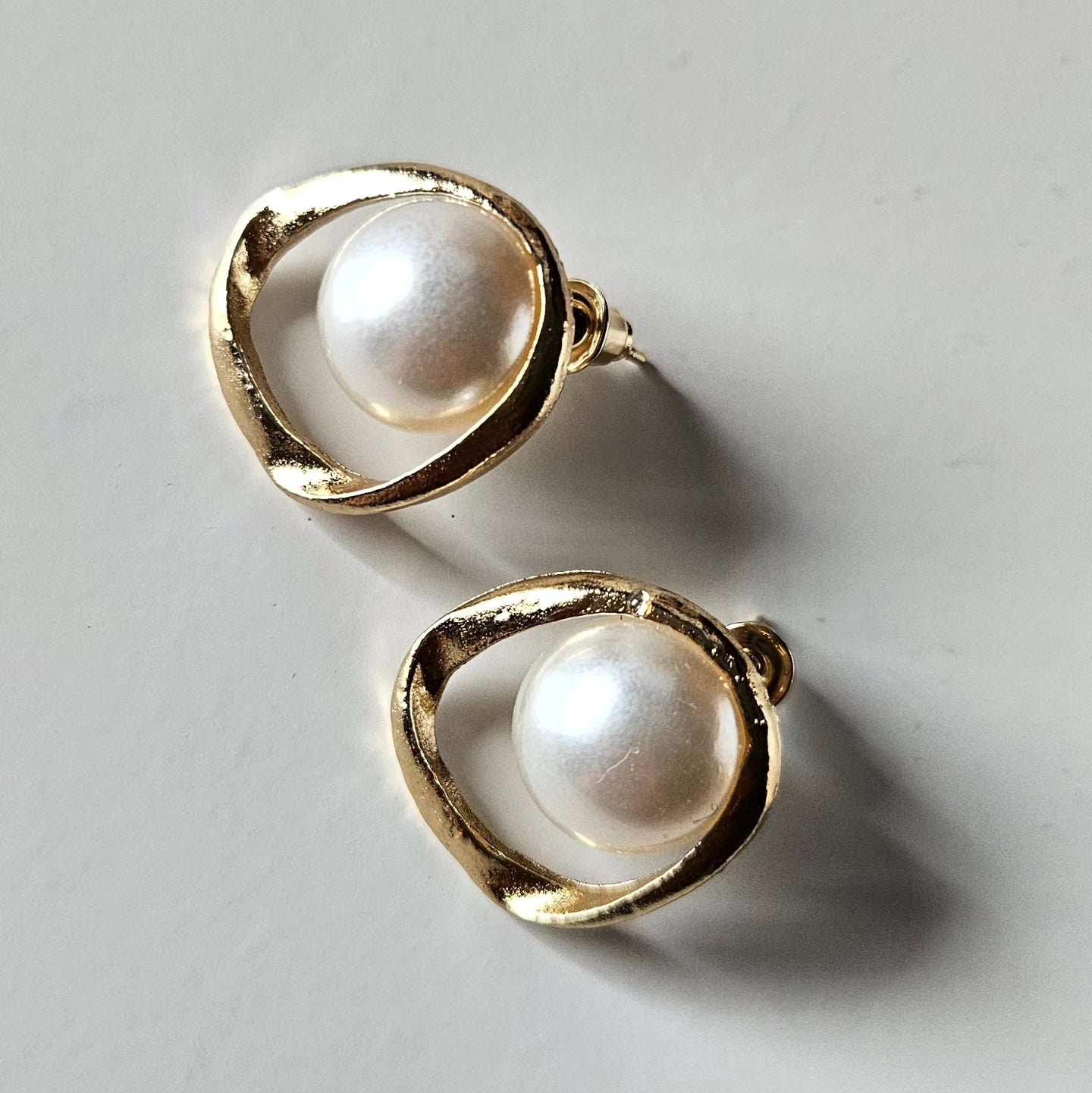 A professional editorial shot of gold and pearl earrings, emphasizing the textured gold finish and the soft glow of the pearls under crisp, high-status brand lighting.