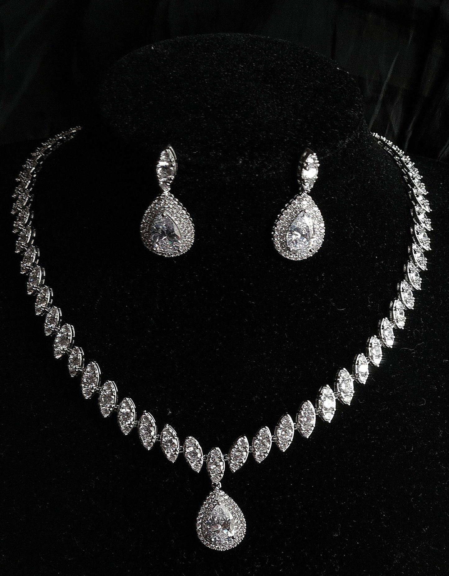 A sophisticated jewelry set on a black velvet display featuring a necklace with marquise diamond links and a prominent pear-cut halo pendant, accompanied by matching teardrop earrings.