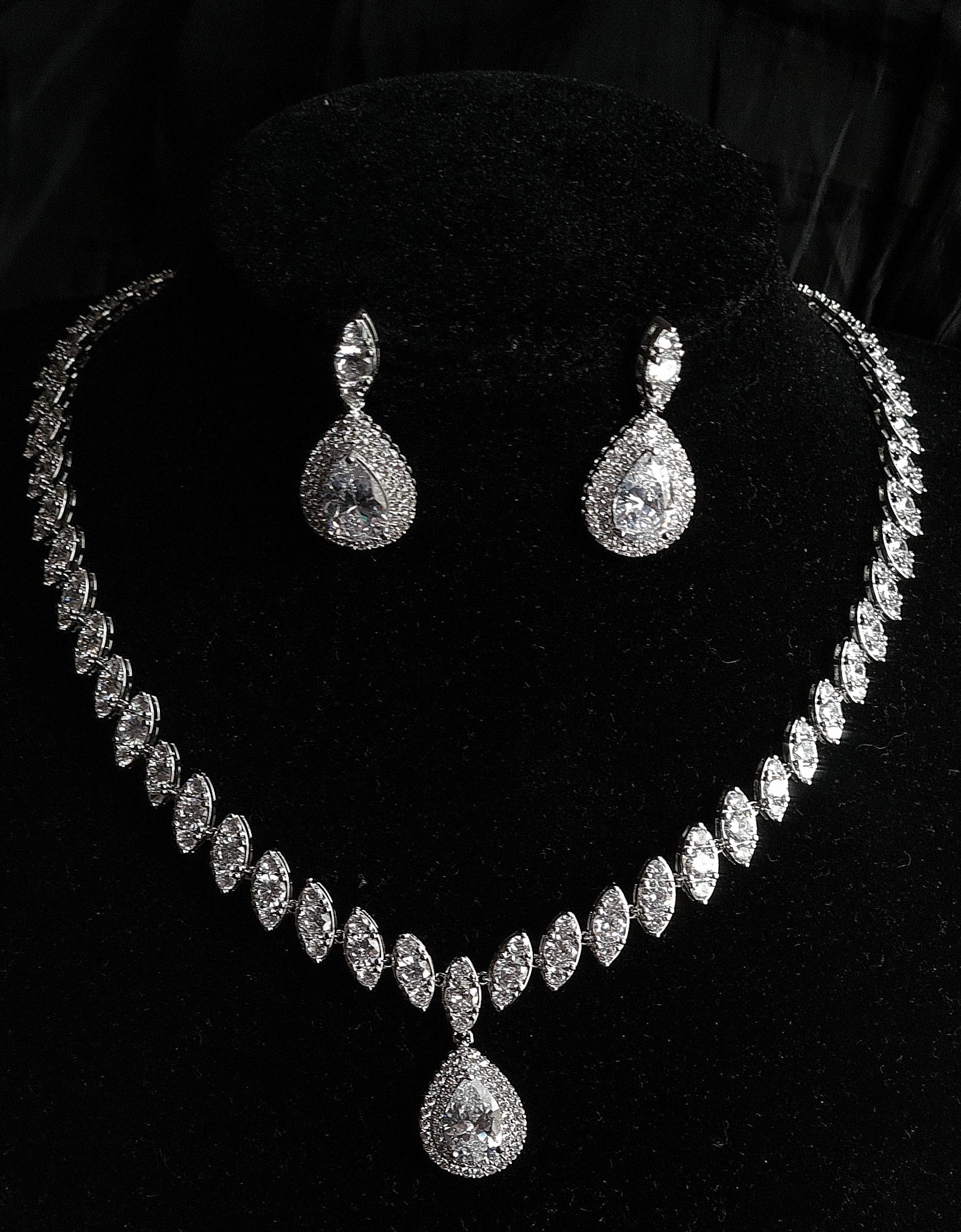 A sophisticated jewelry set on a black velvet display featuring a necklace with marquise diamond links and a prominent pear-cut halo pendant, accompanied by matching teardrop earrings.