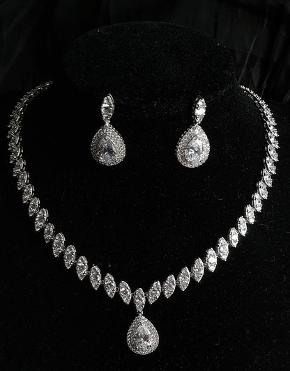 A sophisticated jewelry set on a black velvet display featuring a necklace with marquise diamond links and a prominent pear-cut halo pendant, accompanied by matching teardrop earrings.