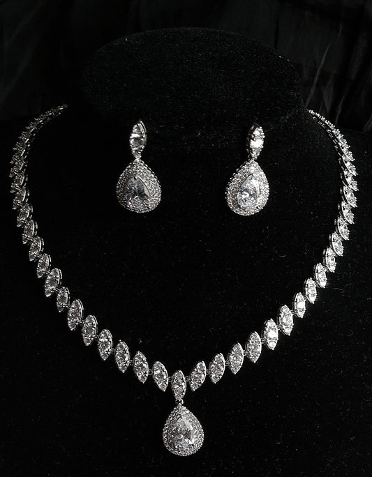 A sophisticated jewelry set on a black velvet display featuring a necklace with marquise diamond links and a prominent pear-cut halo pendant, accompanied by matching teardrop earrings.