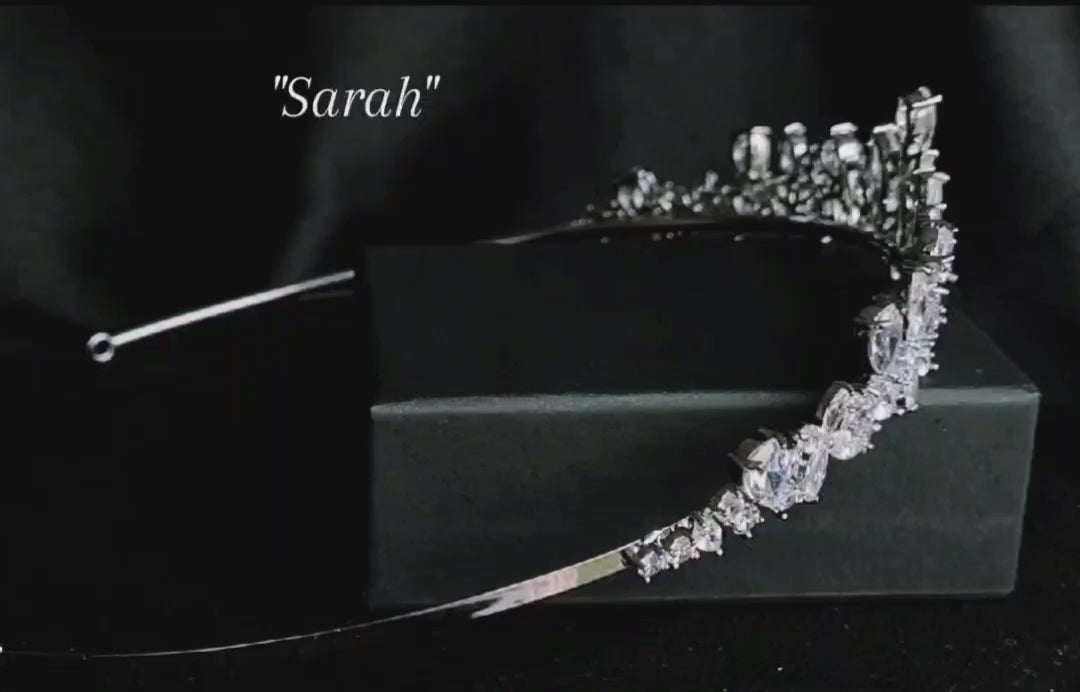 A tiara with diamonds on a black background. The tiara is made of silver and features a delicate design with cascading diamonds. The diamonds are clear and sparkling. The tiara is sitting on a table.