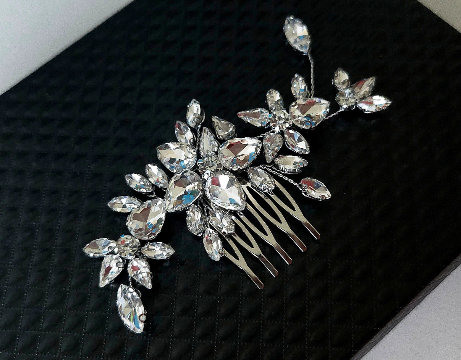 An exquisite Samara bridal hair comb featuring a brilliant cluster of teardrop and marquise-cut crystal gemstones in a floral arrangement, set against a premium black textured backdrop.