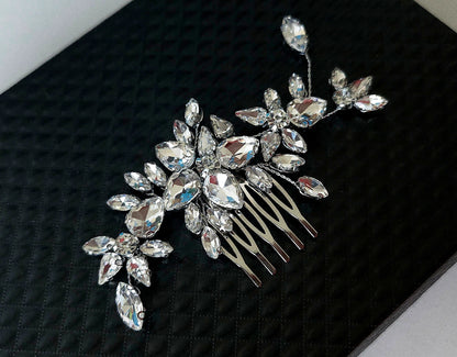 An exquisite Samara bridal hair comb featuring a brilliant cluster of teardrop and marquise-cut crystal gemstones in a floral arrangement, set against a premium black textured backdrop.