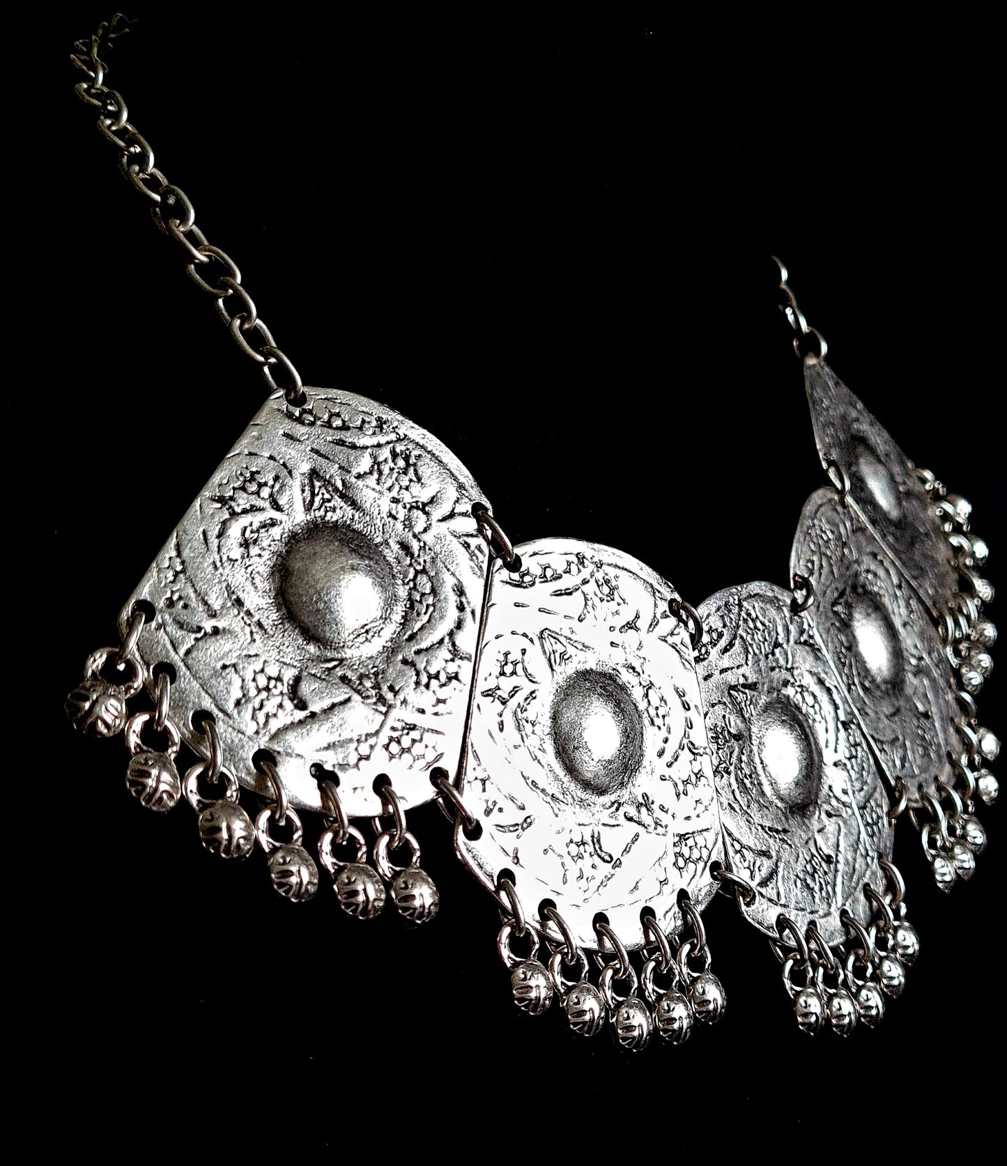 Side profile shot of a bohemian silver statement necklace, highlighting the dimensional engraving of the medallions and the delicate movement of the hanging silver charms.
