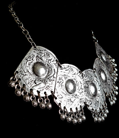 Side profile shot of a bohemian silver statement necklace, highlighting the dimensional engraving of the medallions and the delicate movement of the hanging silver charms.