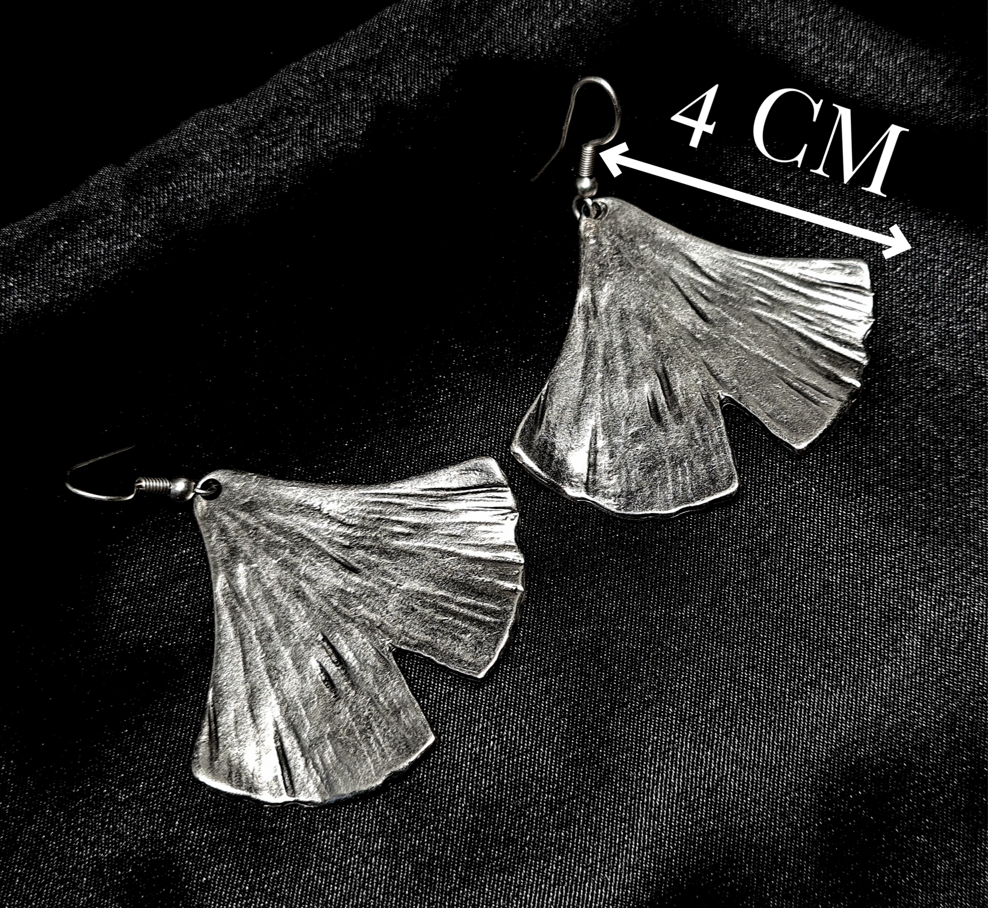Professional studio product shot of ginkgo leaf earrings on a black background with elegant, minimalist white lines showing height and width measurements in millimeters.