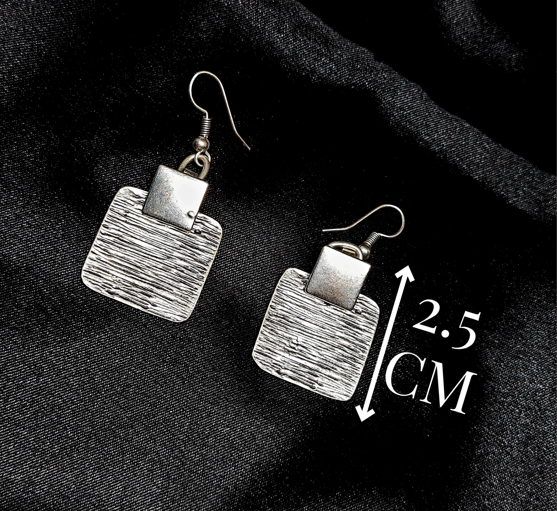 Product specification shot of square silver earrings on a black background with minimalist white lines indicating the height 