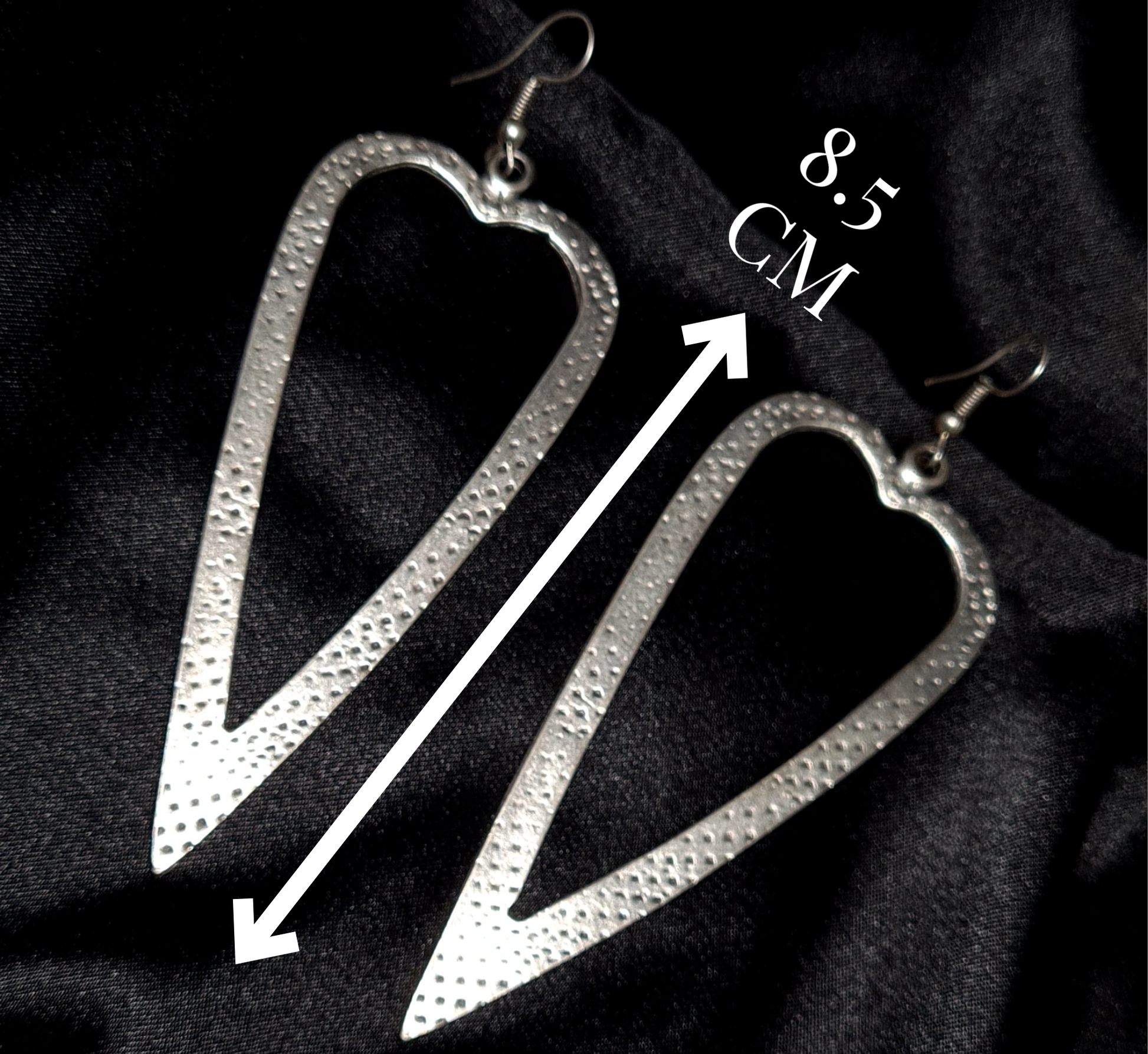 Technical specification layout of silver heart earrings on a black background, with minimalist white lines indicating the 8.5cm drop length.