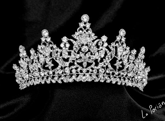 a tiara sitting on top of a black cloth. The tiara is silver in color and has a flower design. The rhinestones are clear and sparkling.