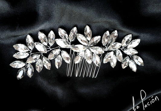 A wedding hair accessory made of silver and rhinestones. The comb is decorated with crystals and has a delicate design.  The comb is sitting on a black cloth.