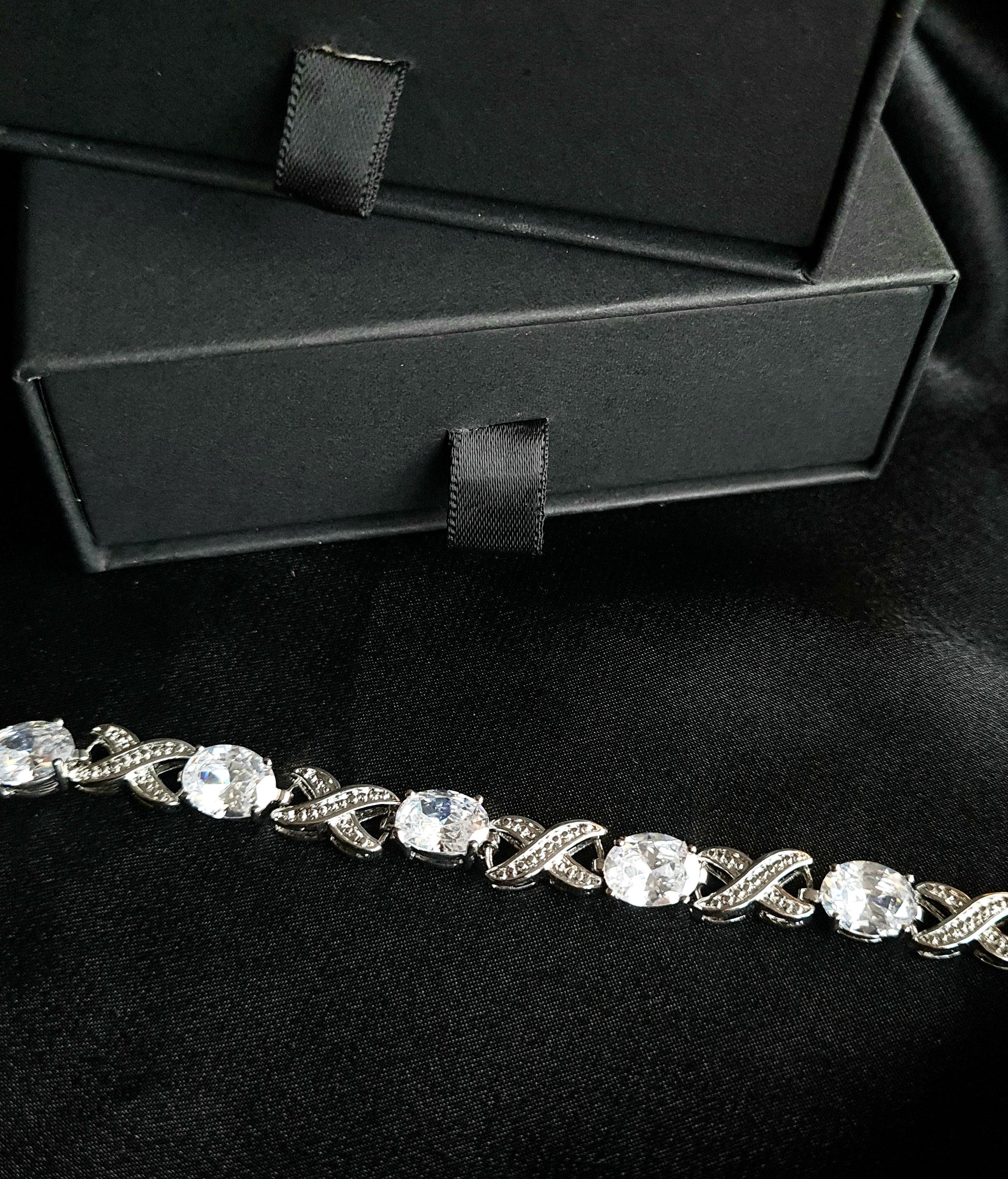 a close up look of a diamond bracelet  sparkling with Cubic Zirconia diamonds in a variety of shapes and sizes. displayed on a black fabric.