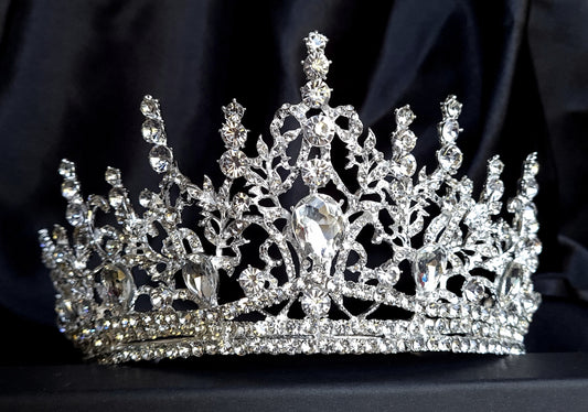 A close-up of a tiara with rhinestones on a black background. The tiara is made of silver and features a delicate design with cascading rhinestones. The rhinestones are clear and sparkling.