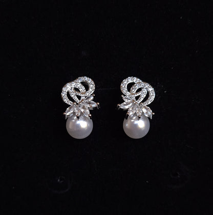 A pair of earrings with a pearl and rhinestones on a black background. The earrings are teardrop-shaped and have a simple, elegant design. The pearl is white and the rhinestones are clear.