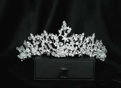 A silver tiara with rhinestones sitting on top of a black box. The tiara is made up of multiple curved bands, each of which is decorated with rhinestones. The tiara is sitting on top of a black box, which is partially obscuring the bottom of the tiara.