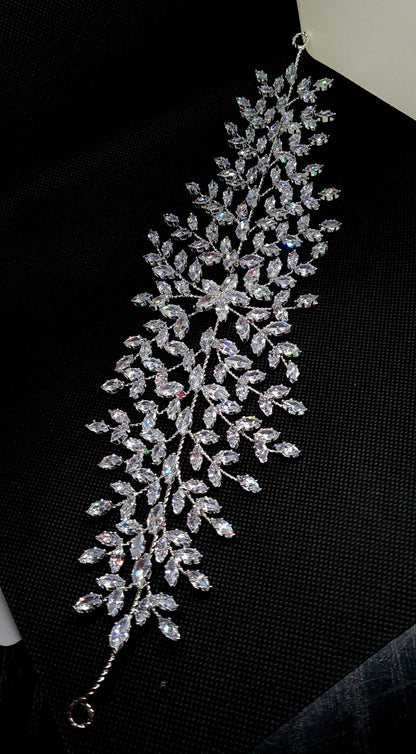 A wedding hair accessory made of metal and diamonds. The tiara has a delicate design with leaves and flowers. The diamonds are clear and sparkling. The background is black.