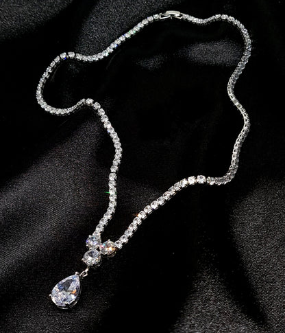 a diamond necklace sparkling with zirconia Diamonds displayed on a black fabric. the necklace is made of on row of cubic zirconia stones the center piece is tear drop shape.