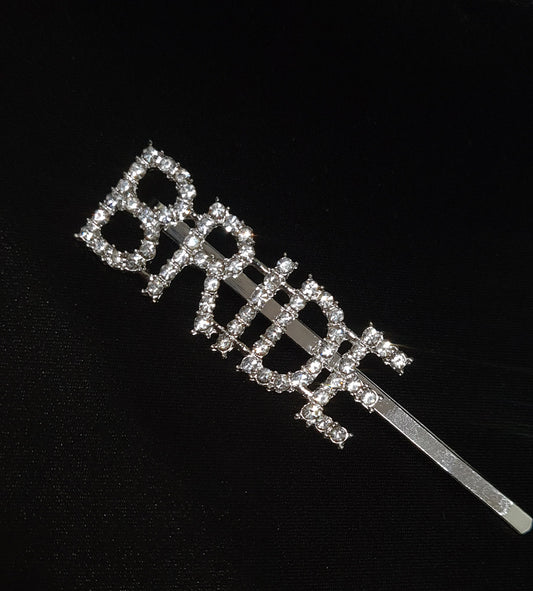  a hair clip with the word "BRIDE" written on it. The hair clip is silver and has a rhinestone border. The word "BRIDE" is in cubic zirconia stones letters