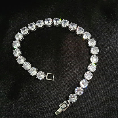 A close-up of a silver bracelet with a single row of diamonds on a black background. The bracelet is simple in design and the diamonds are sparkling.
